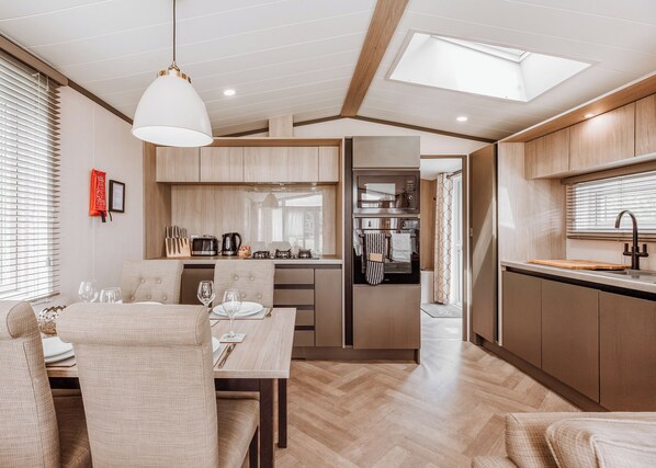 A modern kitchen with wooden cabinets, a dining area with a table and chairs, and a skylight above.