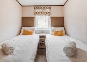 A twin room with two beds, a window with patterned curtains, and a small bedside table.