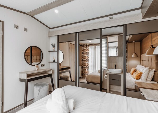 A modern hotel room with a bed, bedside table, mirror, and a view through a sliding door into a bathroom.
