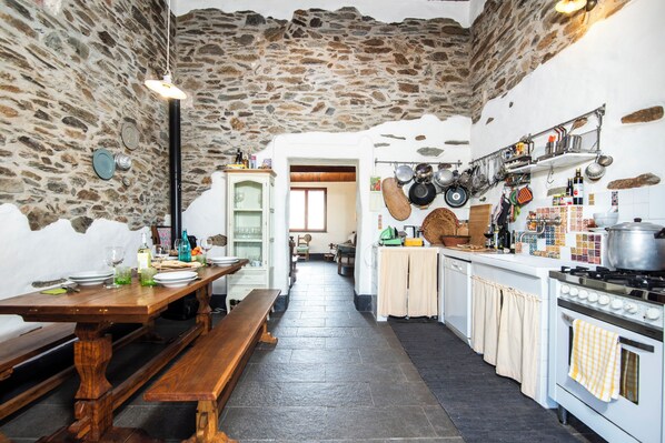 A rustic kitchen with stone walls, a wooden dining table, and a stove.