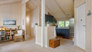 A spacious room with wooden floors and walls, a dining area with a wicker chair and bookshelves, and a kitchen with dark cabinets and a refrigerator. - 2 bedroom gorgeous home in Slagelse (Slagelse)