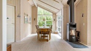 A room with a wooden interior, a dining table with chairs, a large window, and a wood-burning stove. - 2 bedroom gorgeous home in Slagelse (Slagelse)