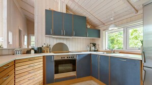 A kitchen with wooden cabinets, a stove, and a window with a view of greenery. - 2 bedroom gorgeous home in Slagelse (Slagelse)
