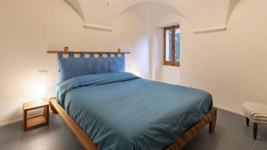 Quarto com uma cama, mesa de cabeceira, janela e luminária pendente.