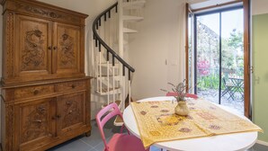 Uma área de refeições com uma mesa branca, uma cadeira rosa, um armário de madeira com entalhes e uma escada em espiral.