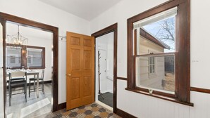 Un couloir avec une porte en bois, un tapis à motifs et une fenêtre donnant sur une maison.