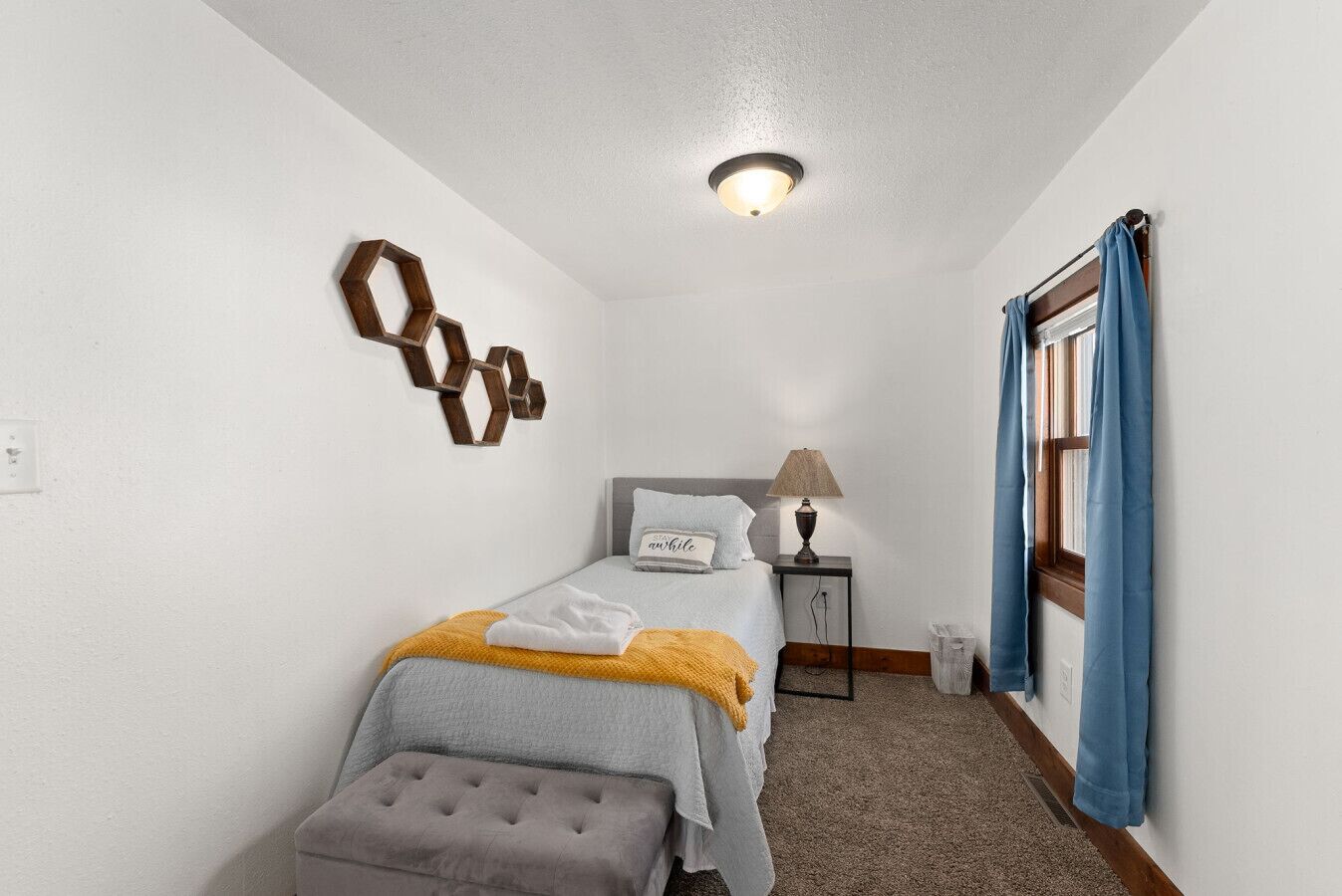 A bedroom with a bed, bedside table, lamp, and a decorative wall piece.