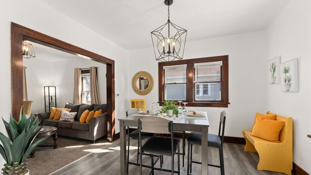 Un salon moderne avec un coin repas, comprenant une table à manger en bois, un canapé avec des coussins, un fauteuil jaune et un grand miroir.