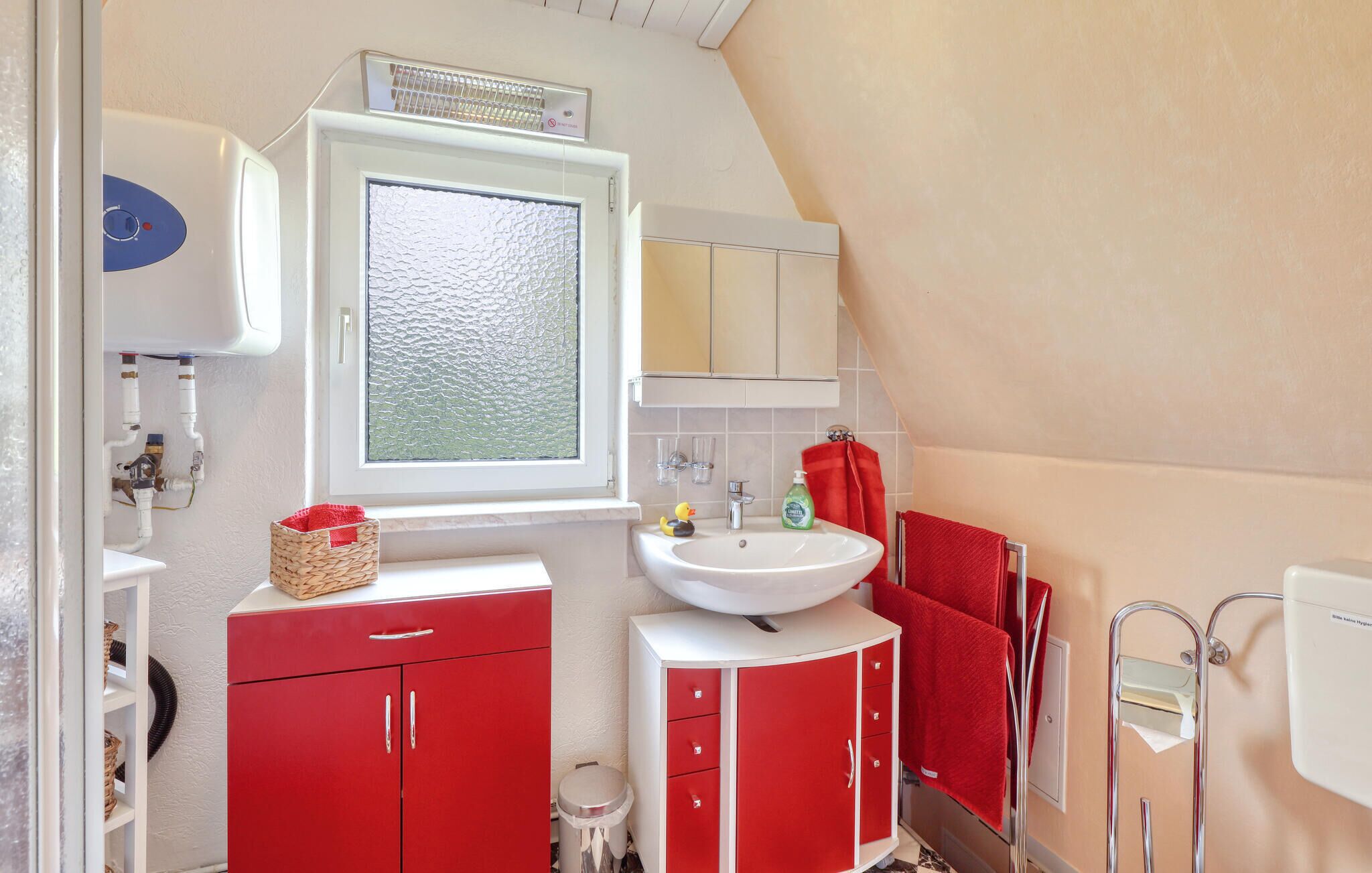 A bathroom with a white sink, red cabinets, a window with frosted glass, and a towel rack.