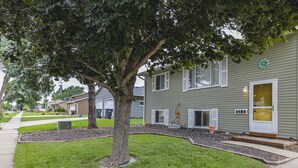 A two-story residential building with a green exterior, a large tree in front, and a well-maintained lawn. - 1 bed 1 bath | Quiet neighborhood (Sioux Falls)