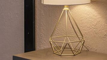 A table lamp with a geometric base and a white lampshade, placed on a table against a textured wall.