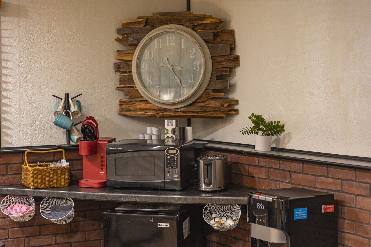A kitchen counter with a coffee maker, toaster, microwave, and a clock mounted on a brick wall.