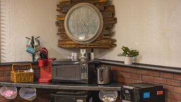 A kitchen counter with a coffee maker, toaster, microwave, and a clock mounted on a brick wall.