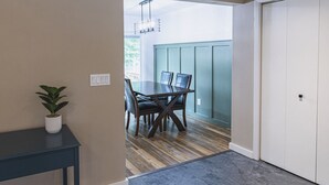 A hallway leading to a dining area with a table and chairs, a potted plant, and a door.