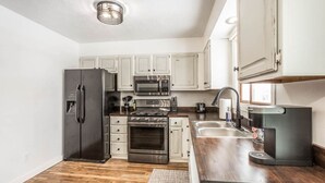 A compact kitchen with white cabinets, stainless steel appliances, and a wooden countertop.