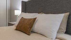 A neatly made bed with a grey headboard, white and brown pillows, and a beige blanket.