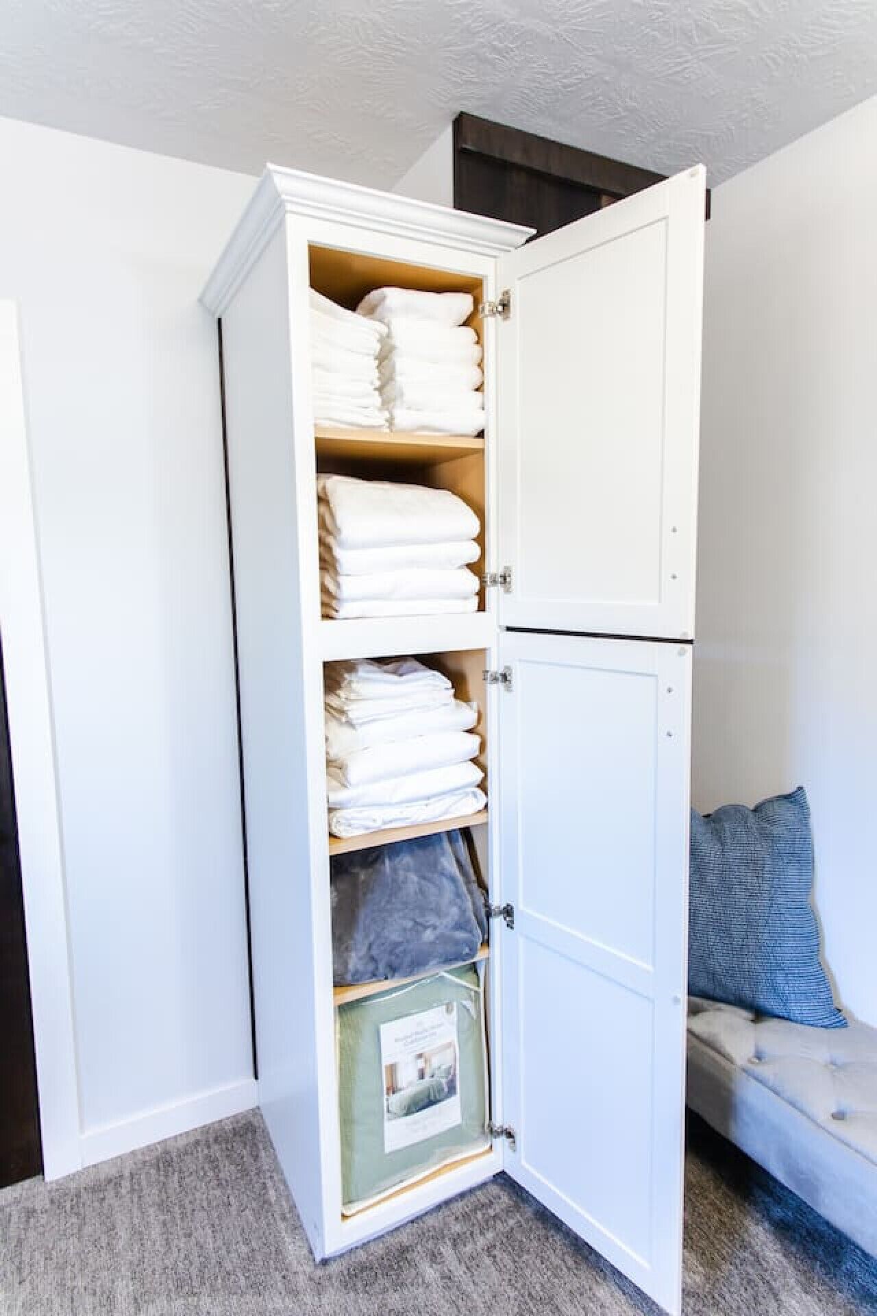 A walk-in closet with multiple shelves for folded clothes, a small storage box, and a door with a handle.