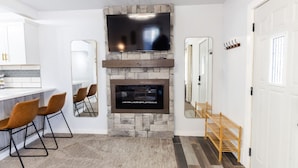 A modern kitchen with a stone fireplace, a flat-screen TV mounted above it, and a bar area with bar stools. - Stylish, comfort-first 2BR/1BA (Sioux Falls)