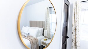 A hotel room with a bed, bedside table, lamp, and a mirror reflecting the room. - Stylish, comfort-first 2BR/1BA (Sioux Falls)