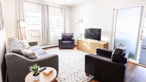Ein modernes Wohnzimmer mit einer Couch, Sesseln, einem Couchtisch, einem Fernseher und einem großen Fenster.