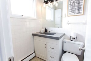 A modern bathroom with a white tiled wall, a gray sink, a white toilet, and a mirror above the sink.
