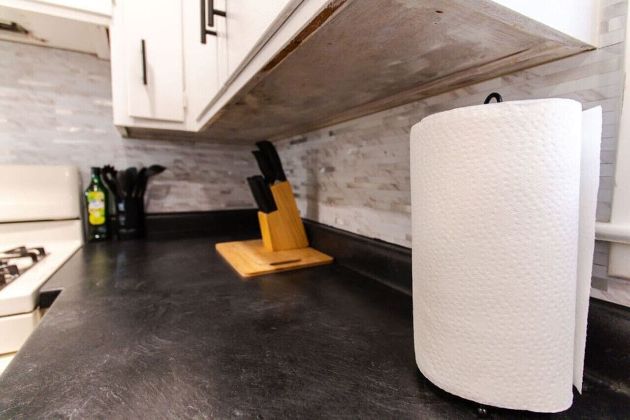 A kitchen counter with a paper towel roll, a knife block, and a bottle of olive oil.
