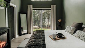 Un dormitorio con una cama grande, una chimenea y vistas a un bosque a través de un ventanal corredero.