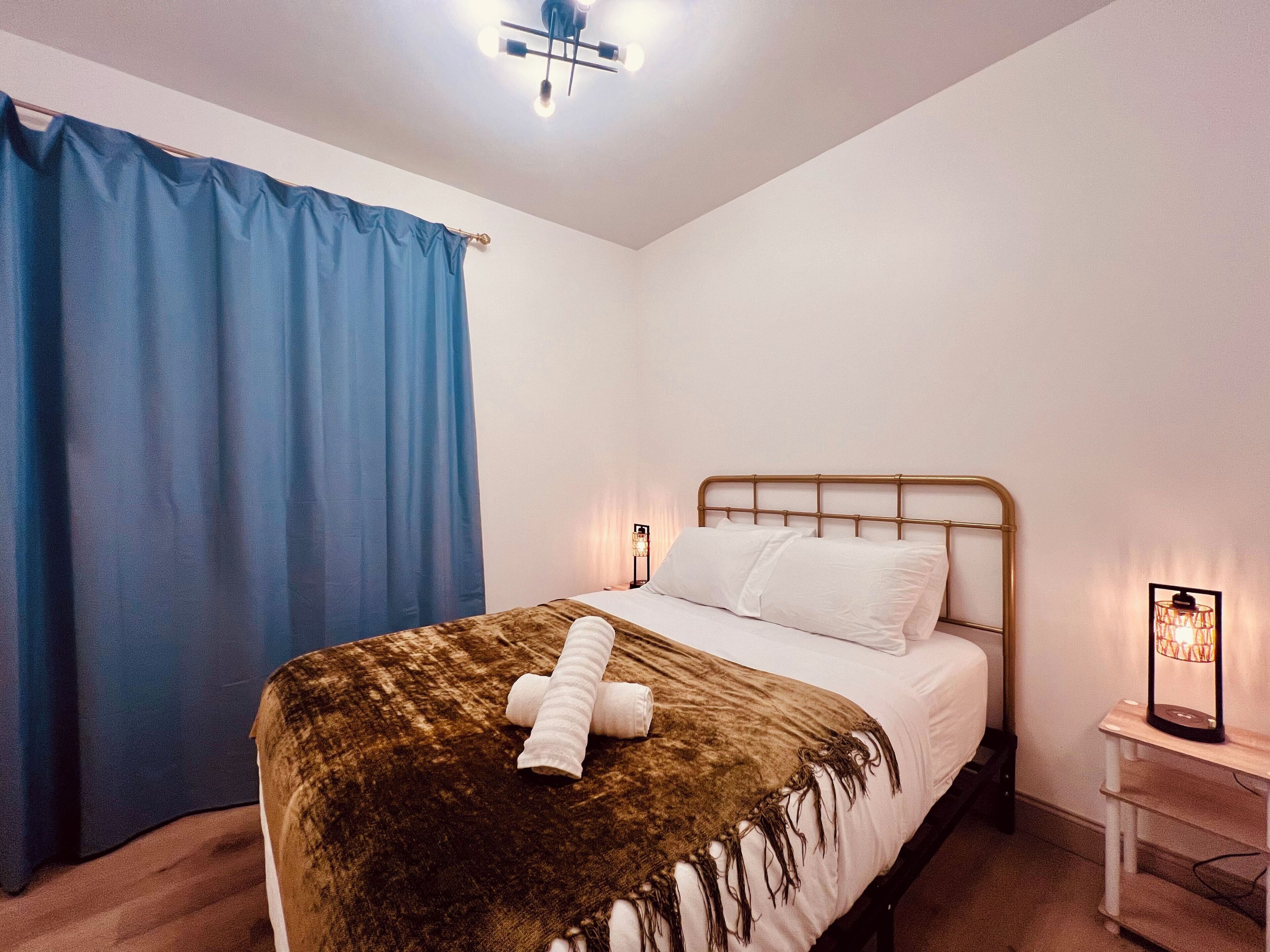 A bedroom with a bed, a nightstand, a lamp, and a blue curtain.