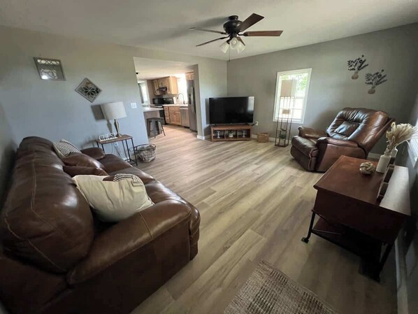 A living room with a brown leather couch, a TV, and a dining area with a table and chairs.