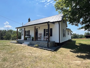 Une maison de plain-pied avec un porche, une cheminée et un petit jardin devant.