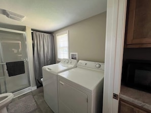 Une buanderie équipée d’un lave-linge et d’un sèche-linge, d’un espace douche et d’une fenêtre avec des rideaux.