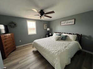 A bedroom with a bed, dresser, ceiling fan, and a wall with a framed sign. - Country cottage near lake! (Monticello)