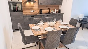 A modern kitchen with a wooden countertop, built-in cabinets, and a dining area with a wooden table and grey upholstered chairs. - Sunshine view 3 by Interhome (Reifnitz)