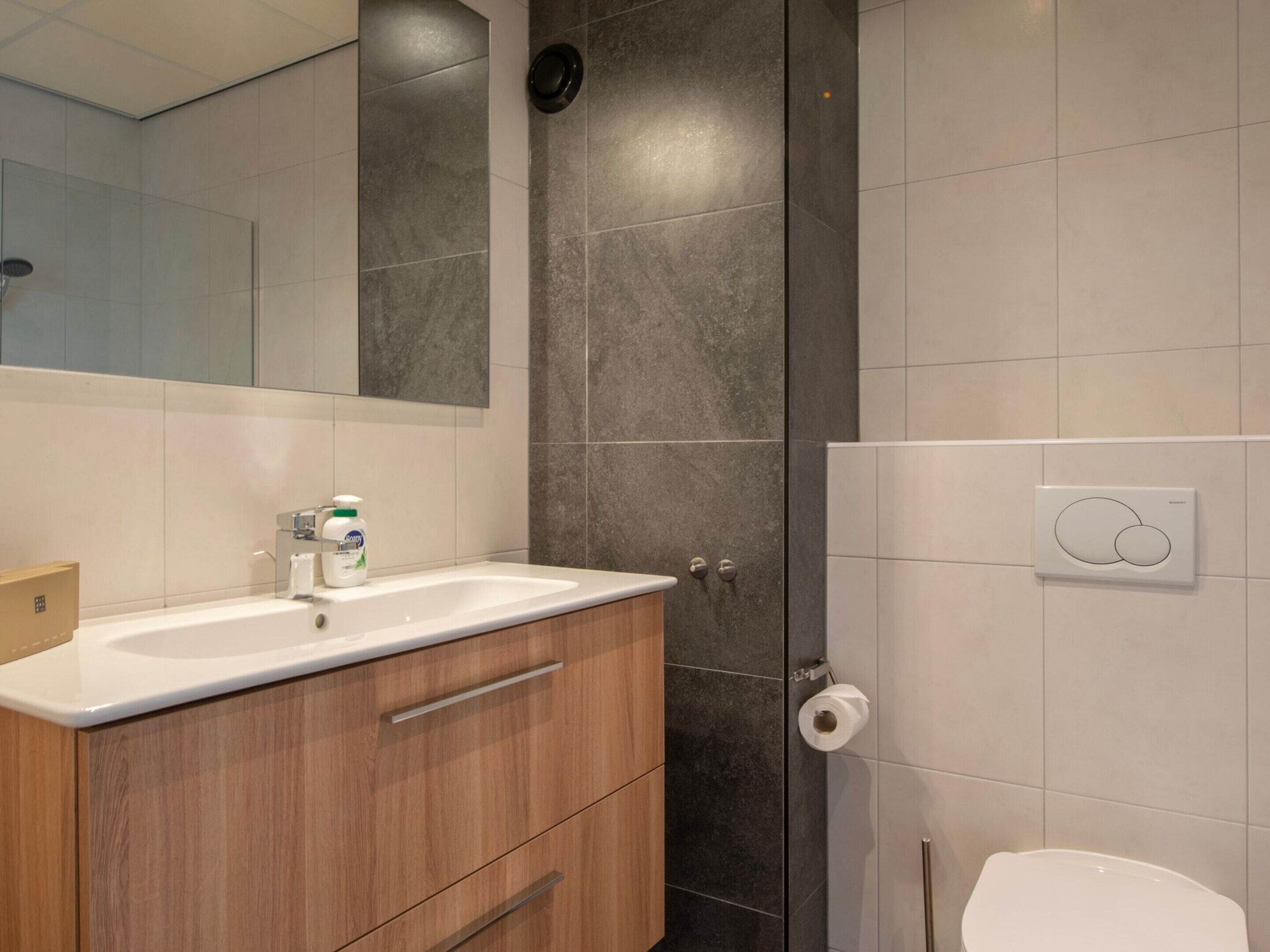 Un baño moderno con tocador de madera, ducha e inodoro.