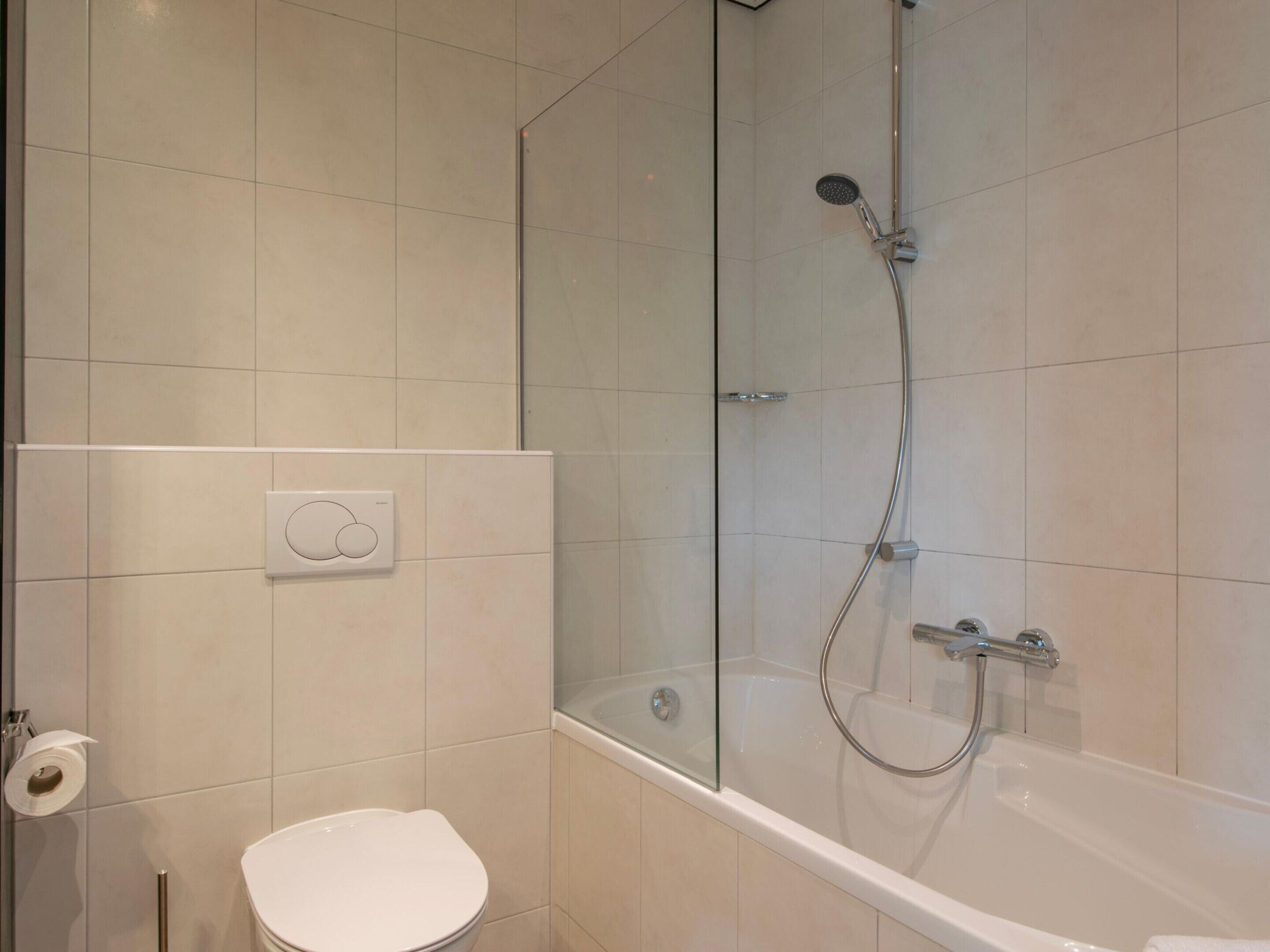 A bathroom with a toilet, a glass-enclosed shower, and a bathtub.