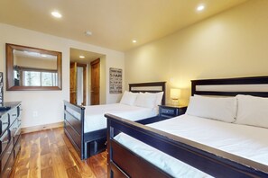 A hotel room with two beds, wooden flooring, a dresser, a mirror, and a wall sign.