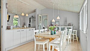 Una cocina amplia con armarios blancos, una mesa de comedor de madera y lámparas colgantes.