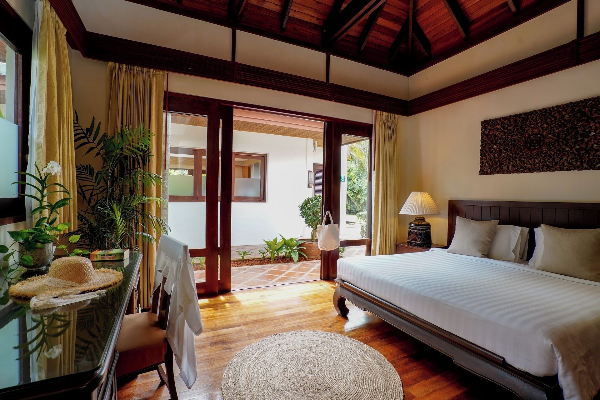 A bedroom with a bed, a desk with a chair, a lamp, and a potted plant.