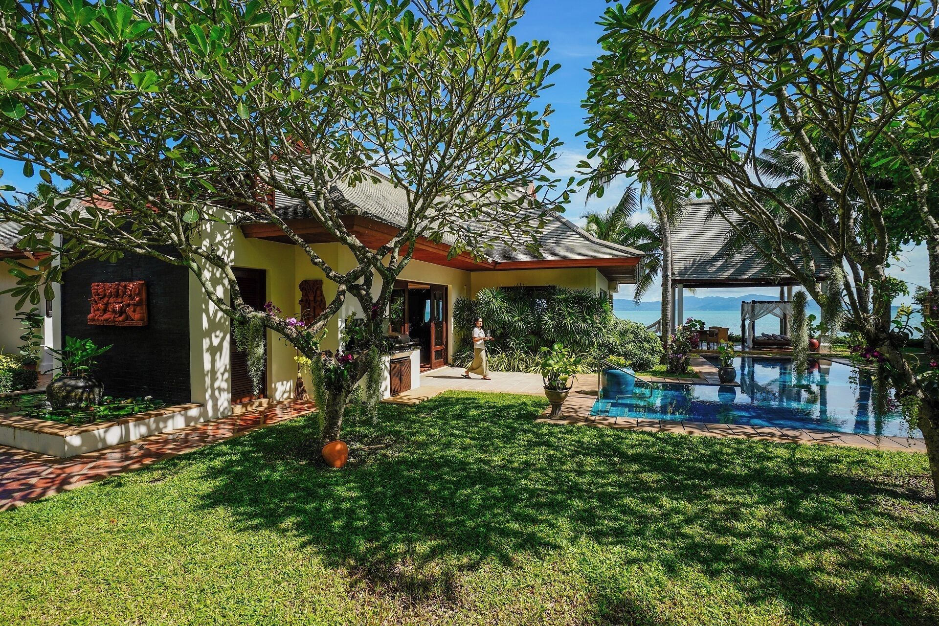 A house with a swimming pool, surrounded by lush greenery and a clear view of the ocean.