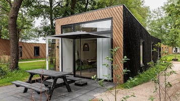 A modern, compact building with a wooden exterior and large glass doors, featuring a picnic table outside.