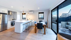 A modern kitchen with a central island, stainless steel appliances, and a dining area with a large window overlooking a deck. - Mountain View Haven T (Wanaka)