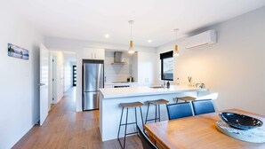 A modern kitchen with a central island, bar stools, and a dining table with a decorative bowl. - Mountain View Haven T (Wanaka)