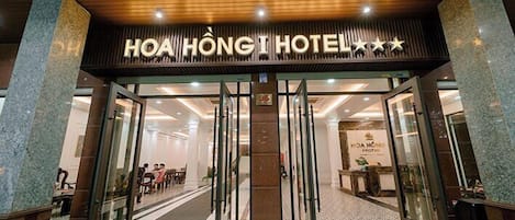 The entrance of Hoa HONG HOTEL with a modern design, featuring glass doors and a wooden ceiling.