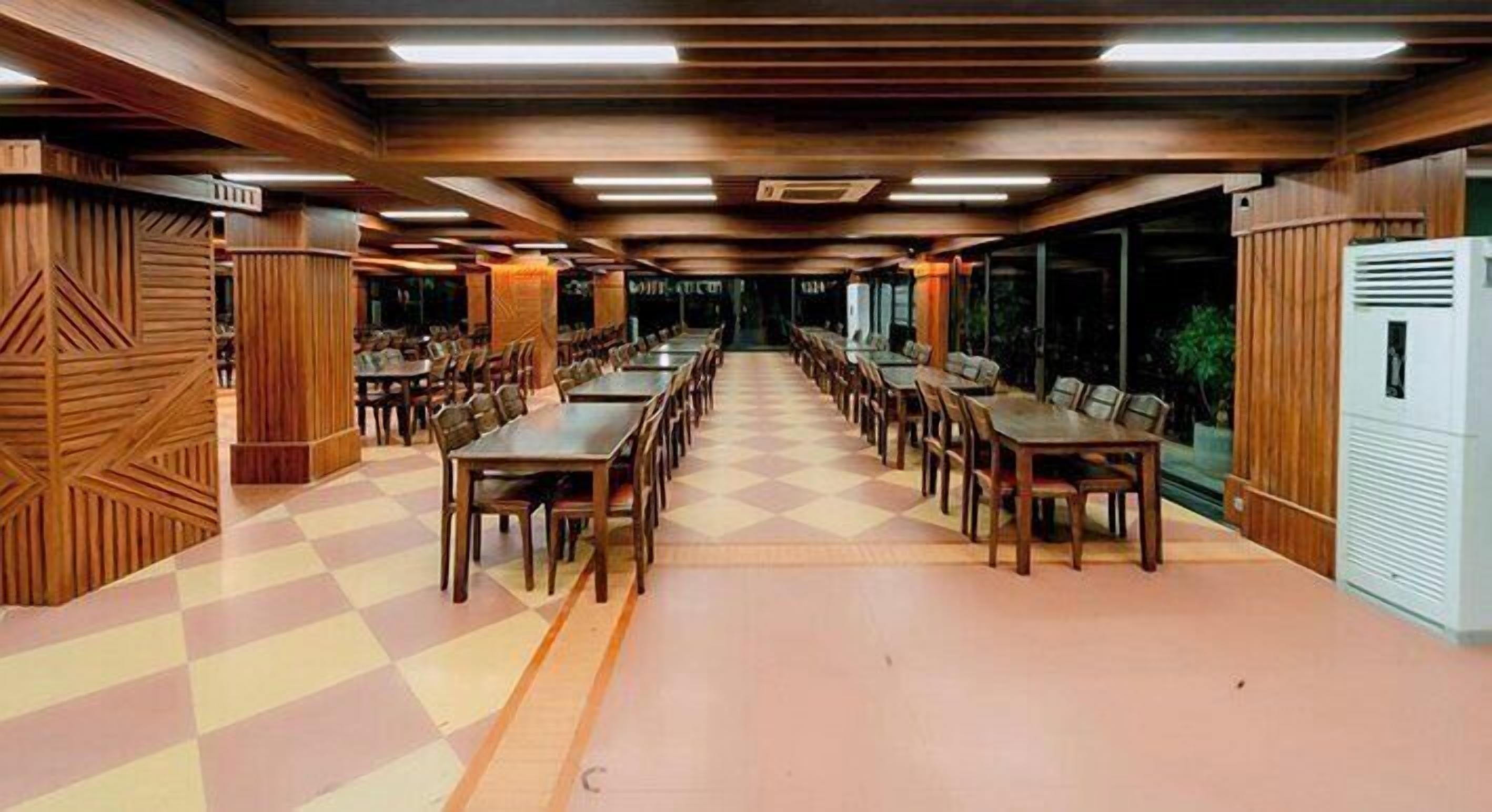 Un amplio comedor con largas mesas y sillas, paneles de madera en las paredes y un piso con diseño de cuadros.