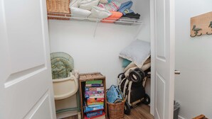 Een kleine, rommelige opbergruimte met planken, manden en een kinderwagen.