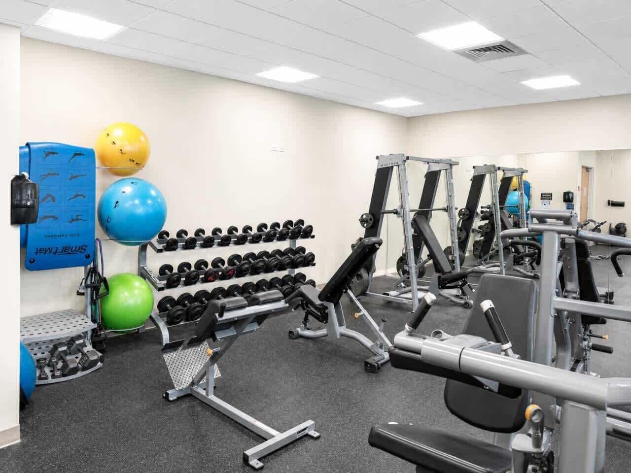 A gym with various exercise equipment, including dumbbells, exercise balls, and weight machines.