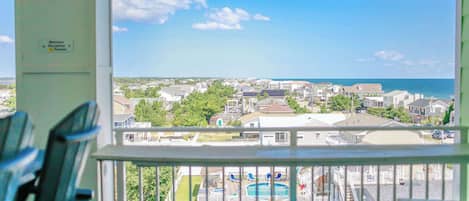 Une vue depuis un balcon donnant sur une piscine et agrémenté de chaises, avec en arrière-plan un quartier résidentiel avec des maisons et un ciel dégagé.