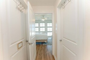 A hallway leading to a bedroom with a bed, a ceiling fan, and a window with multiple panes. - Sojourns Beach Views & Pool Family Home Sleeps 9 (Virginia Beach)