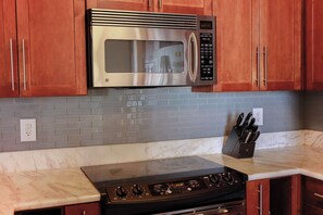 A kitchen with a stainless steel microwave, a black stove, wooden cabinets, a marble countertop, and a knife block.