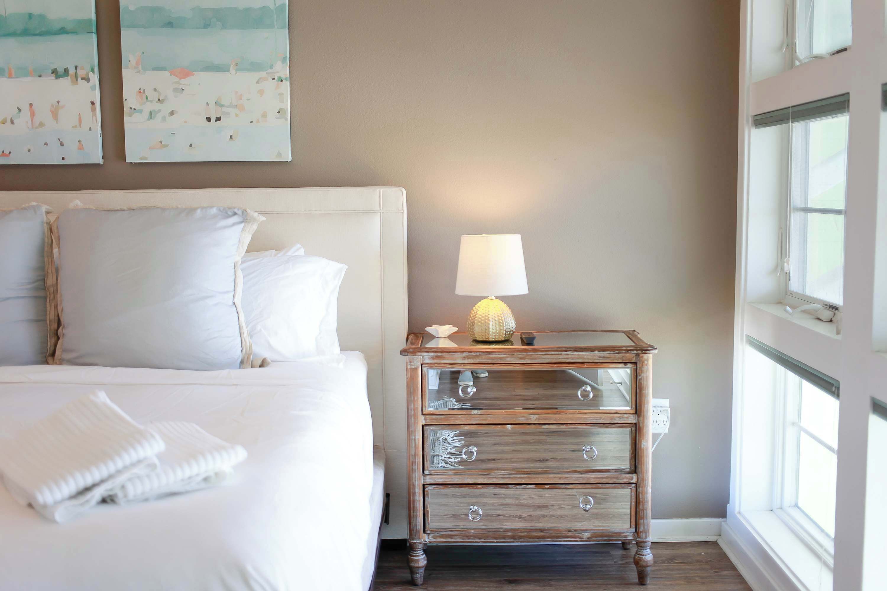A bedroom with a bed, bedside table, lamp, and artwork on the wall.